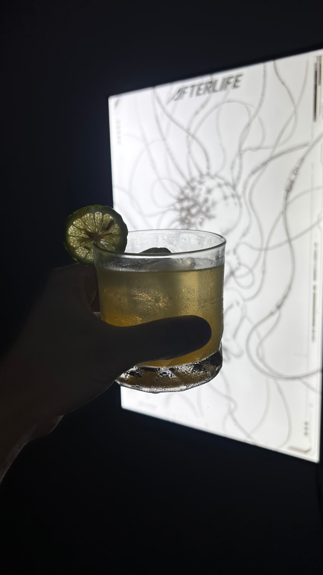 Hand holding a cocktail in front of an Afterlife poster